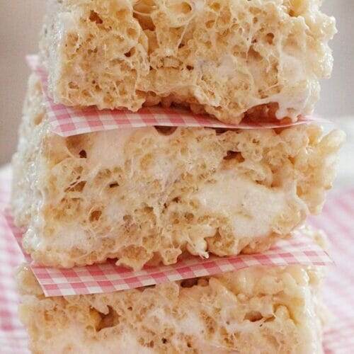 Three thick Perfect Rice Krispies Treats stacked on top of each other, separated by squares of parchment paper.