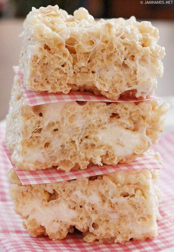 Three thick Perfect Rice Krispies Treats stacked on top of each other, separated by squares of parchment paper.