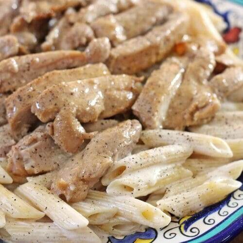 Large serving platter with a bed of alfredo penne pasta and sliced Cajun ranch chicken on top.