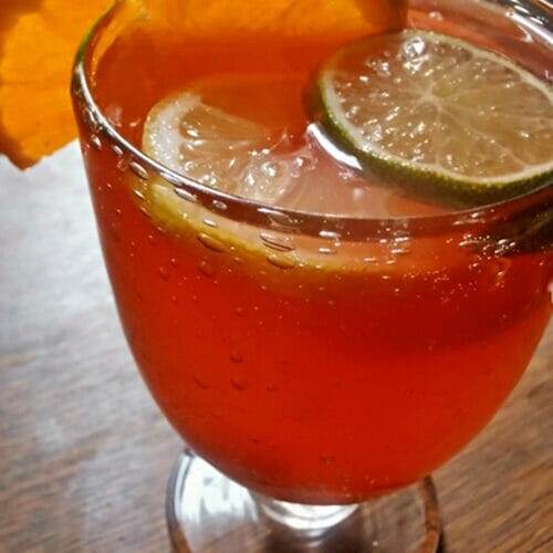 Large glass cup filled with a red sangria punch with cherries, orange, lemon and lime slices.