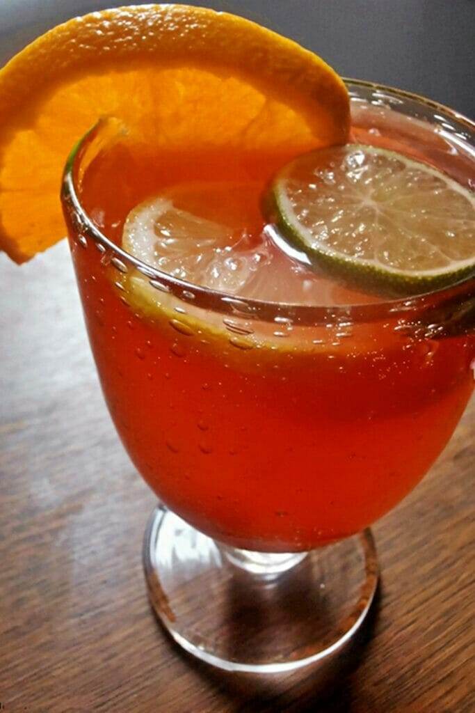 Large glass cup filled with a red sangria punch with cherries, orange, lemon and lime slices.