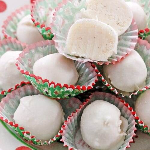A red and white polka dot dish piled high with white eggnog truffles, each truffle in a red and green holiday candy liner.