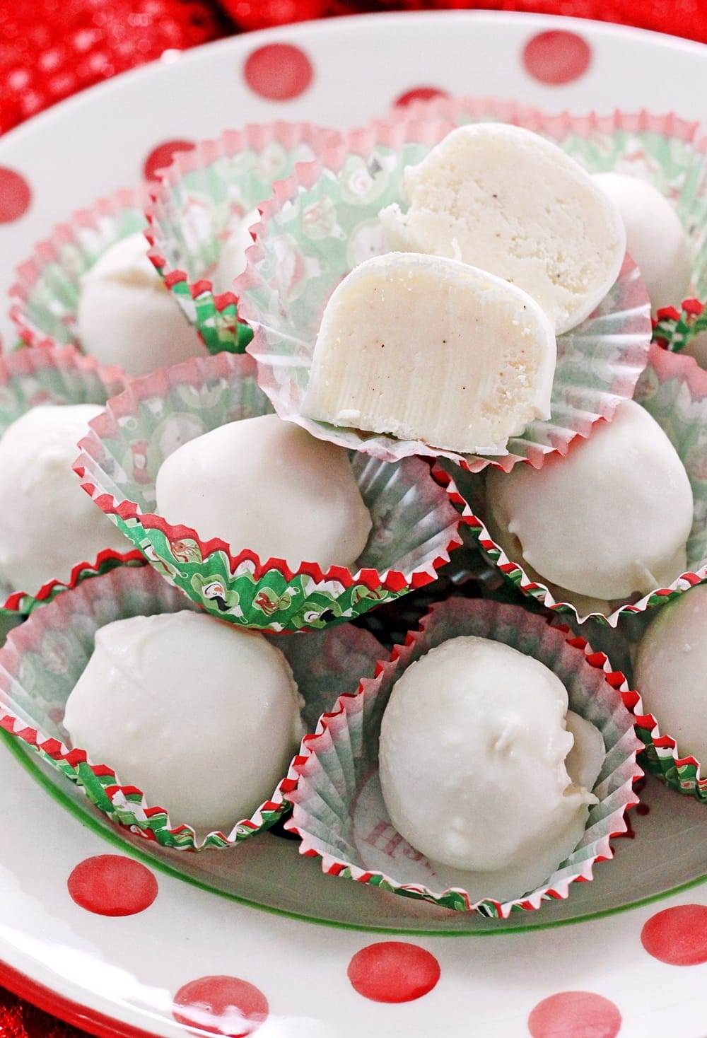 A red and white polka dot dish piled high with white eggnog truffles, each truffle in a red and green holiday candy liner.