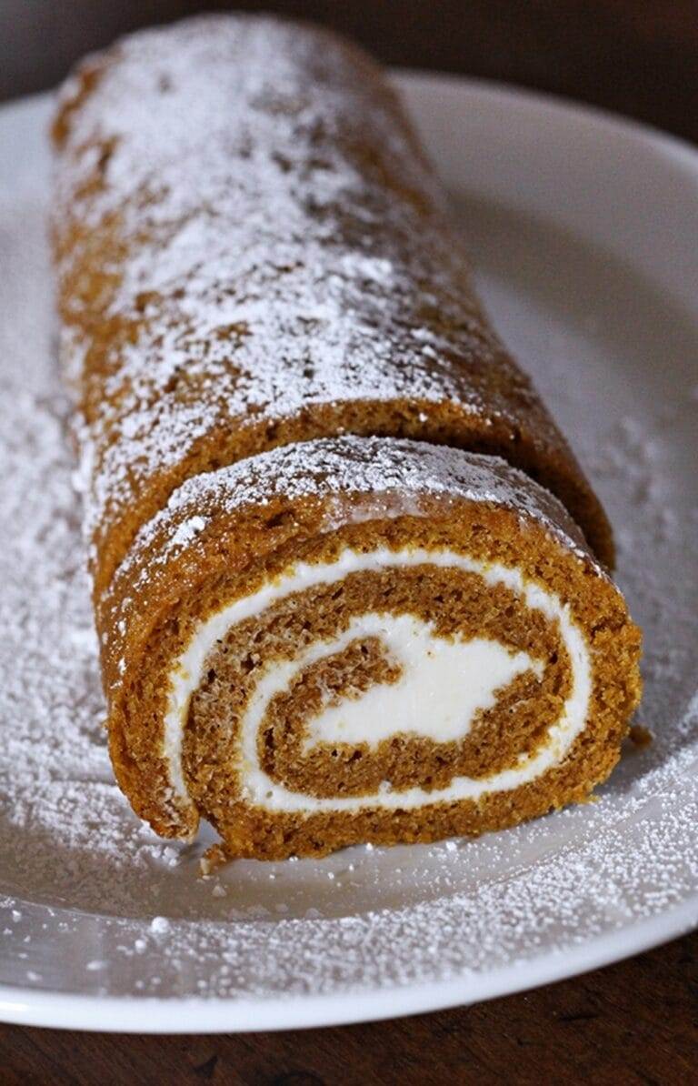 A pumpkin roll in a cylindrical shape, with one piece cut to see the cross section. Filled with a sweet cream cheese filling.